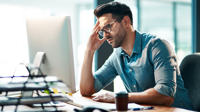 homem sentado à secretária com ar preocupado a fazer contas